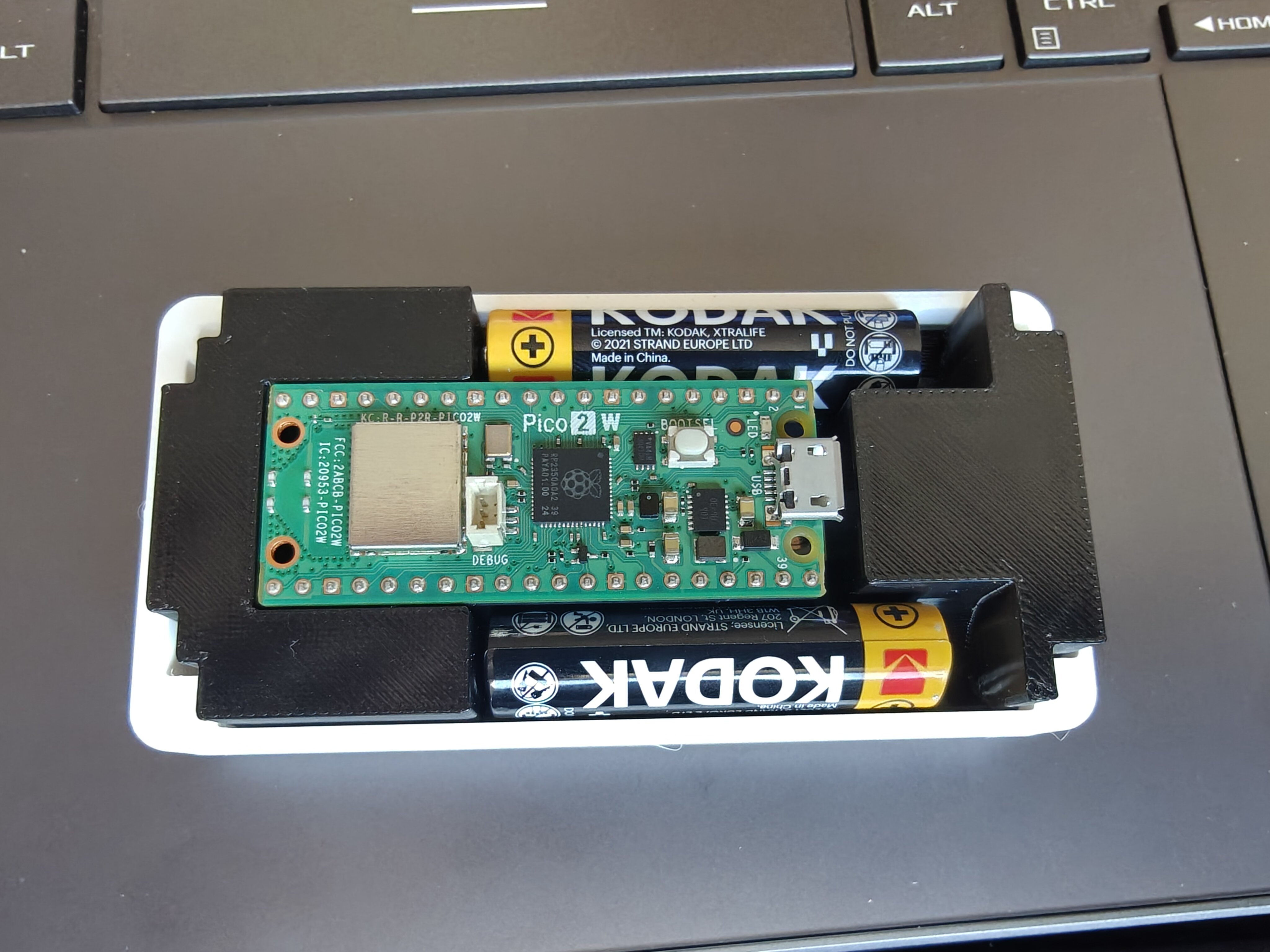 Assembled cradle in base plate — top-down with Pico 2 W and dual AAA cells