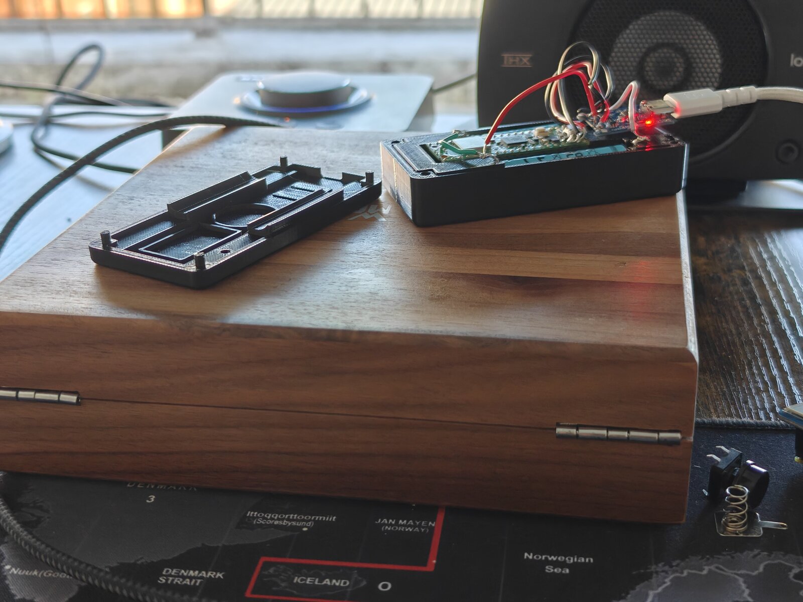 NoSolar case opened — base plate separated, showing Pico W and battery inside the black case with TP4056 charging LED red