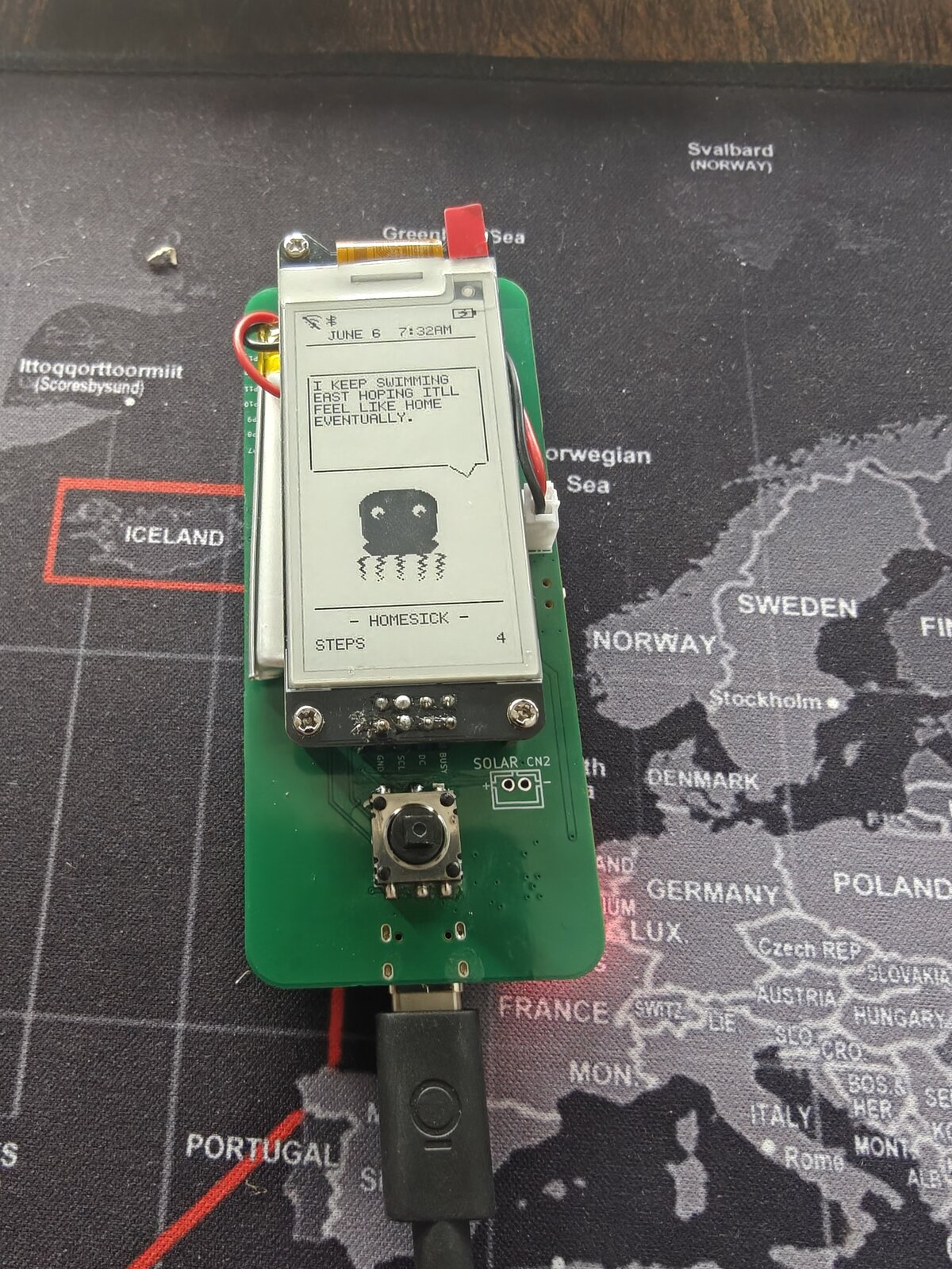 Dilder Board in tall portrait orientation — speech-bubble quote "I KEEP SWIMMING EAST HOPING IT'LL FEEL LIKE HOME EVENTUALLY." above a HOMESICK octopus, STEPS 4, Bluetooth icon lit