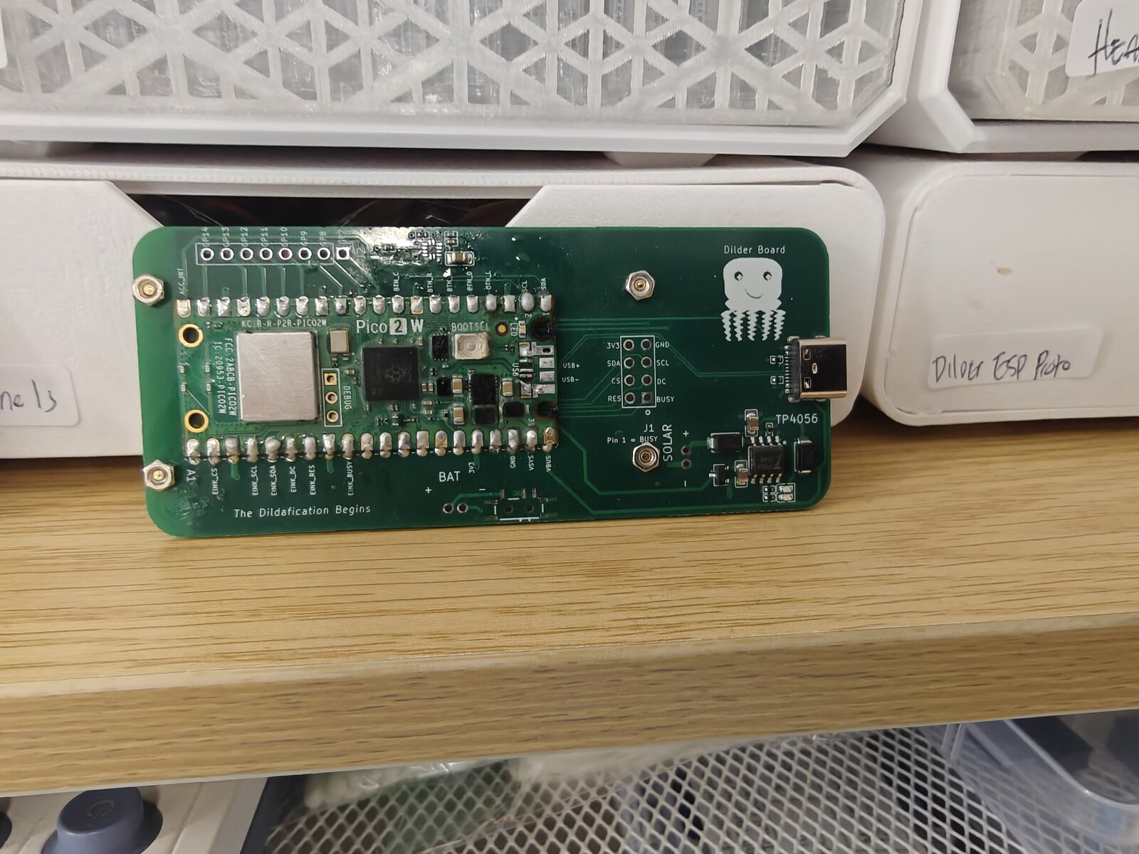Bare custom Dilder Board — green PCB with Raspberry Pi Pico 2 W, TP4056 charger, solar pads, and the octopus silkscreen reading "Dilder Board"