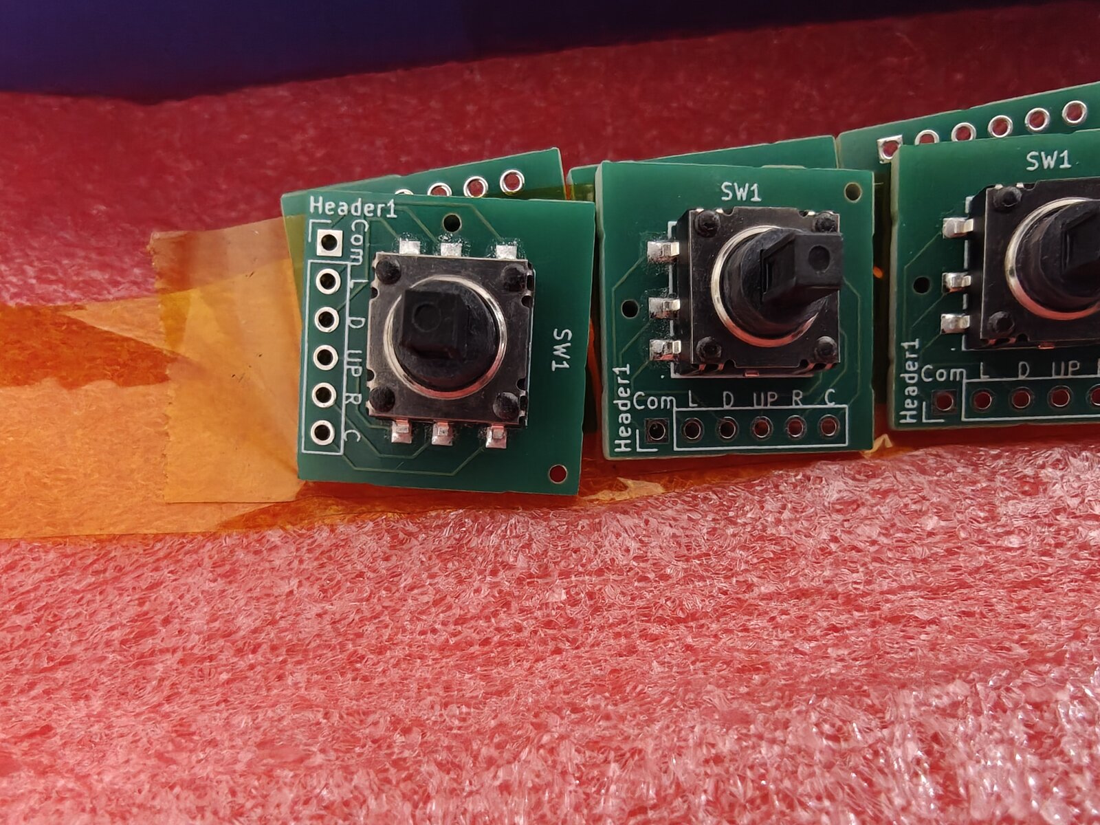 Macro closeup of individual joystick breakout boards showing Header1, Com, L, D, UP, R, C silkscreen labels and SW1 switch
